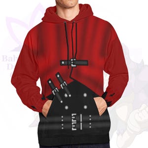 May include: Red hooded sweatshirt with a black graphic design on the front. The design includes a black pocket, black straps, and white dots. The sweatshirt has a drawstring and a kangaroo pocket.