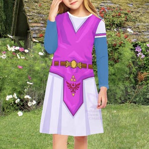 Peut inclure: Une robe à manches longues avec un corsage rose vif orné d'une ceinture marron imprimée et d'une boucle dorée. La jupe est blanche avec un panneau central rose affichant un blason rouge et or. Les manches sont bleues avec des poignets blancs.