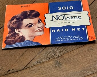 May include: Vintage Solo Nolastic Hair Net packaging. The orange and blue package features a smiling woman with blonde hair. Text includes "Hair Net" and "Made of Rayon".