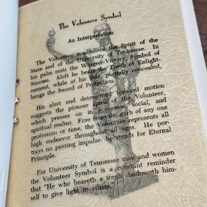 May include: Open book page with text and a drawing of a statue. The text reads "The Volunteer Symbol" and describes the symbol's meaning for the University of Tennessee. The drawing is a sketch of a person holding a torch.