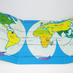 May include: A blue and white world map with continents outlined in yellow, green, and pink. The map is divided into three sections, with the Arctic Circle, Equator, and Antarctic Circle marked. The map also includes the names of the continents and oceans.