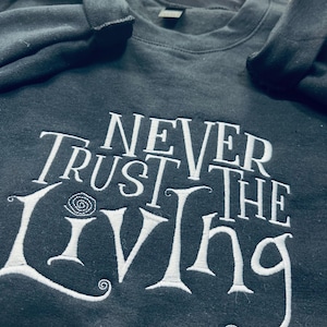 Pu&ograve; includere: Felpa nera con testo ricamato bianco che recita "Never Trust the Living".