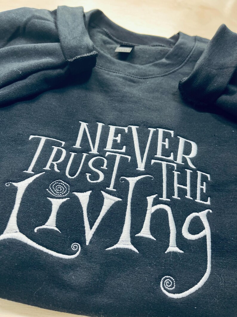 Pu&ograve; includere: Felpa nera con testo ricamato bianco che recita "Never Trust the Living".