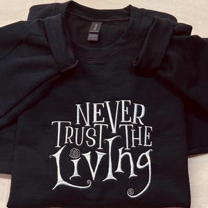 Pu&ograve; includere: Felpa nera con testo ricamato in bianco che recita "Never Trust the Living".