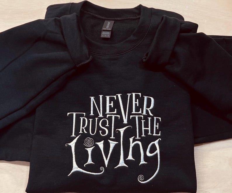 Pu&ograve; includere: Felpa nera con testo ricamato in bianco che recita "Never Trust the Living".
