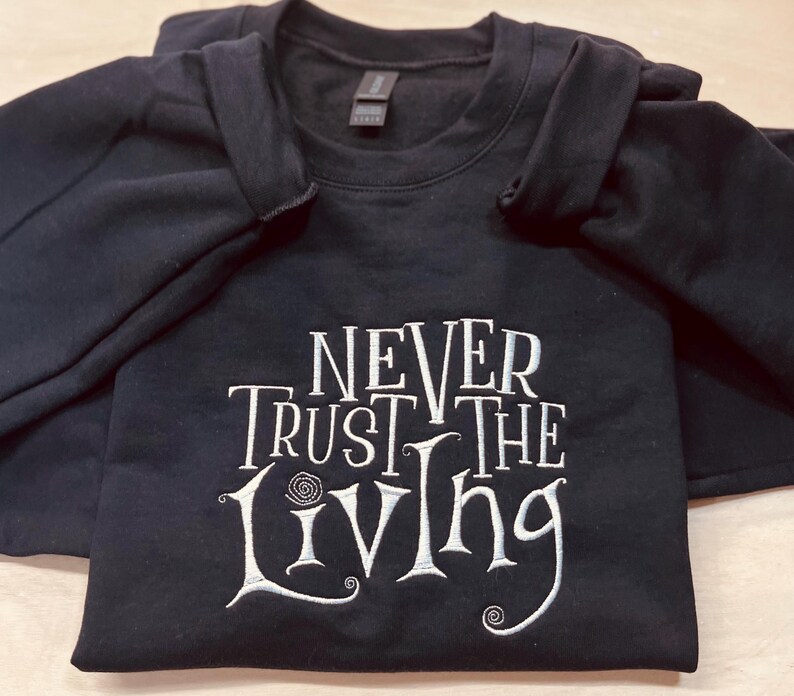 Pu&ograve; includere: Felpa nera con testo ricamato in bianco che recita "Never Trust the Living".