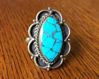 May include: A turquoise ring with a silver setting. The turquoise is a bright blue color and has a marbled pattern. The setting is a silver oval with a decorative border.