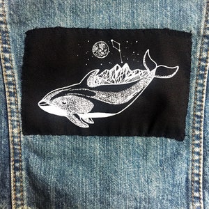 May include: A black patch with a white outline of a dolphin carrying a mountain range on its back. The dolphin is swimming towards the left side of the patch. There is a small white circle with a star inside, and a flag with a star on top of the mountain range.