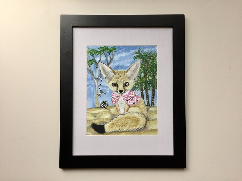 May include: A framed watercolor painting of a fennec fox wearing a pink and white patterned shirt. The fox is sitting in a desert landscape with palm trees and a blue sky.