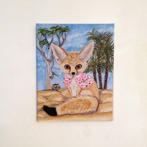 May include: A painting of a fennec fox wearing a pink and white patterned scarf. The fox is sitting in a desert scene with palm trees and a blue sky.