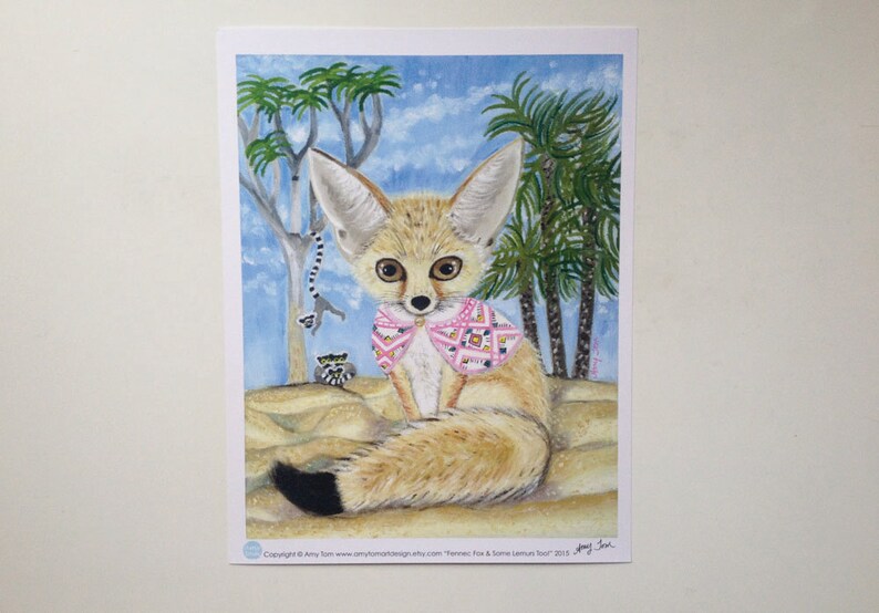 May include: A painting of a fennec fox wearing a pink and white patterned scarf. The fox is sitting on sand with palm trees in the background. The painting is signed "Amy Tom" and dated "2015".