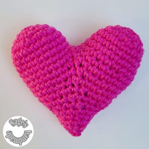 May include: A pink crocheted heart-shaped pillow. The pillow is made with a soft, textured yarn and has a slightly bumpy surface.