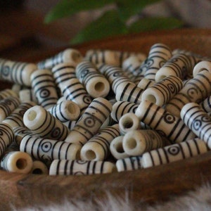 Puede incluir: Un cuenco de madera lleno de cuentas cilíndricas blancas con diseños geométricos negros. Las cuentas están dispuestas en un patrón aleatorio.