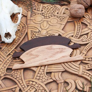 May include: A carved wooden board with intricate patterns, featuring a skull, two wooden objects, walnuts, and peacock feathers. The board has a light brown color, and the wooden objects are dark brown and light brown.