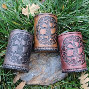 May include: Three leather cups with a tree of life design. The cups are brown, black, and red.