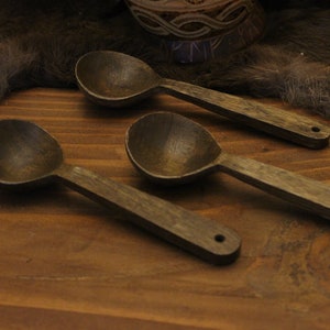May include: Three wooden spoons with dark brown stain, lying on a wooden surface. The spoons have a rounded bowl and a long handle.