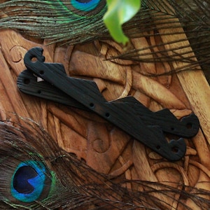 May include: Two black wooden decorative pieces with a unique shape, possibly for a craft project, rest on a carved wooden surface. Peacock feathers with blue and green accents add a touch of color.
