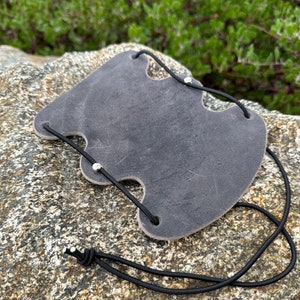 May include: A gray leather archery arm guard with black elastic straps and silver rivets.