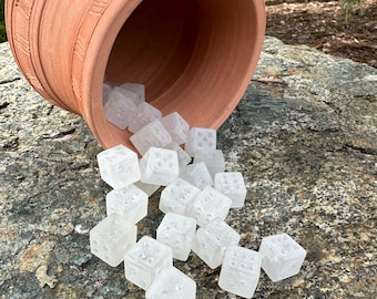 Könnte beinhalten: Ein umgestürzter Topf aus terrakottafarbener Keramik, der klare, würfelförmige Würfel auf eine strukturierte Felsfläche verschüttet. Die Würfel haben kleine, eingekerbte Punkte, die Zahlen darstellen. Der Topf hat ein geriffeltes Design um seinen Rand.
