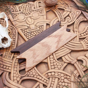 Op de afbeelding: Een houten carving met ingewikkelde ontwerpen, met een klein houten pijlvormig stuk erop. De carving is bruin en heeft een natuurlijke houten afwerking.