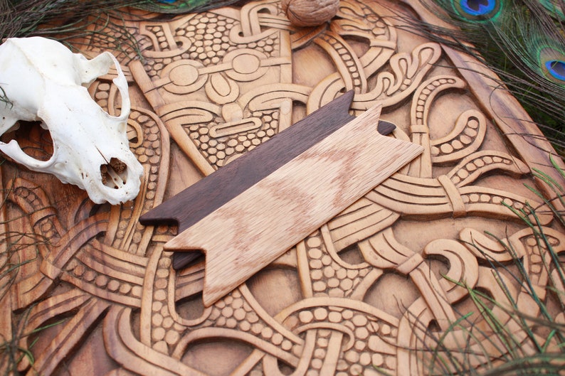 Op de afbeelding: Een houten carving met ingewikkelde ontwerpen, met een klein houten pijlvormig stuk erop. De carving is bruin en heeft een natuurlijke houten afwerking.