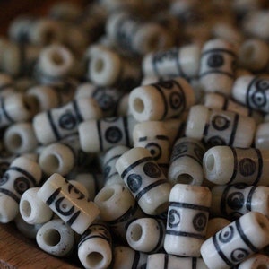 May include: A bowl filled with white cylindrical beads with black geometric designs. The beads are arranged in a random pattern.