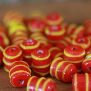 May include: A close-up of a pile of red and yellow striped glass beads. The beads are arranged in a random pattern and are all the same size.