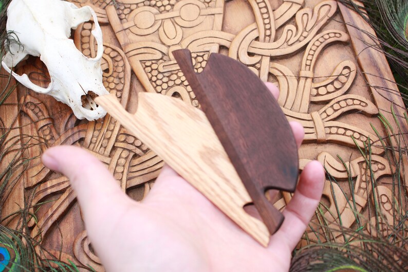 May include: Two wooden, hand-carved bottle openers. One is light-colored, the other is dark brown. The openers are held over a carved wooden surface with a skull in the background. The background has a carved, Celtic knot design.
