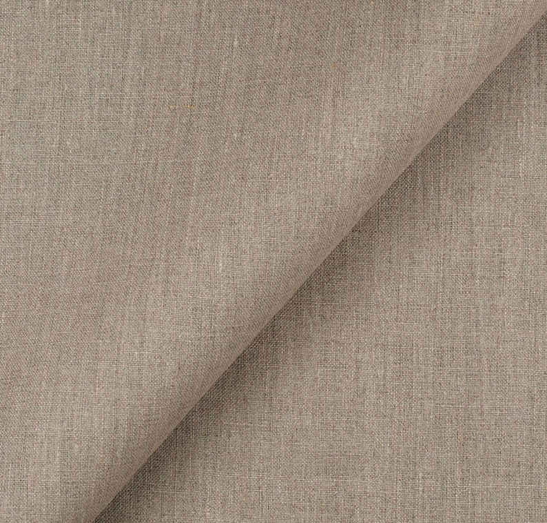 Puede incluir: Primer plano de una tela de lino beige con una textura sutil tejida. La tela est&aacute; doblada por la mitad, creando una l&iacute;nea diagonal a trav&eacute;s de la imagen.