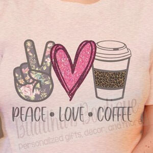 May include: A pink t-shirt with a peace sign, heart, and coffee cup graphic. The peace sign is floral patterned, the heart is pink glitter, and the coffee cup has a leopard print band. The text "Peace Love Coffee" is below the graphic.