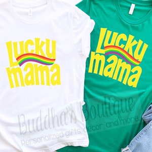 May include: Two t-shirts with the text "Lucky Mama" in yellow letters with a rainbow arc above the text. The t-shirts are white and green.