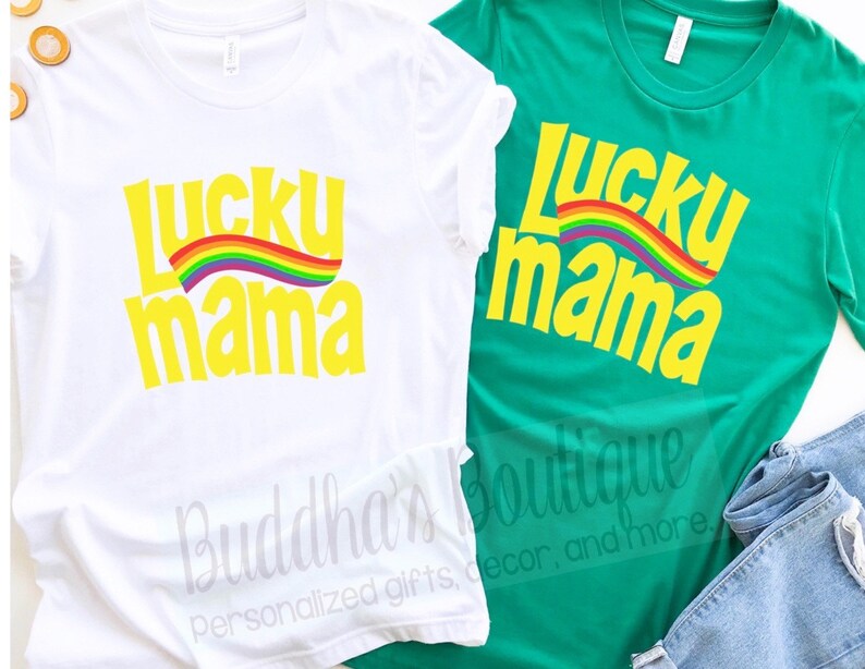 May include: Two t-shirts with the text "Lucky Mama" in yellow letters with a rainbow arc above the text. The t-shirts are white and green.