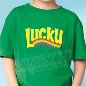 May include: Green t-shirt with a yellow "Lucky" graphic and a rainbow arc. The text "Buddha's Boutique Personalized gifts, decor, and more" is visible in the bottom right corner.