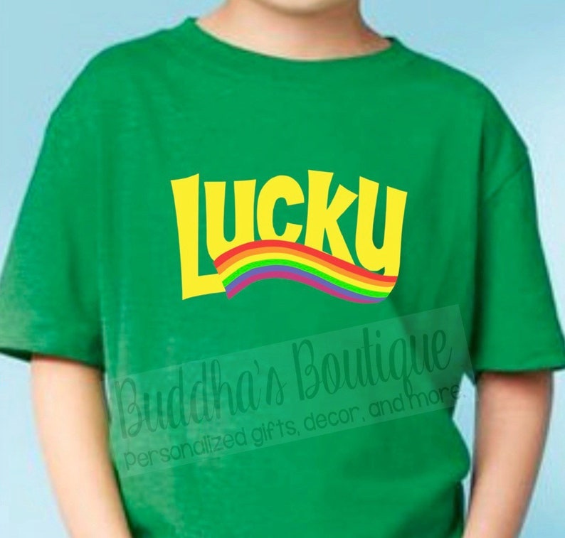 May include: Green t-shirt with a yellow "Lucky" graphic and a rainbow arc. The text "Buddha's Boutique Personalized gifts, decor, and more" is visible in the bottom right corner.