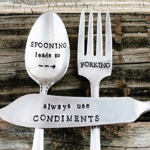 May include: Three silver utensils with engraved sayings. A spoon reads "SPOONING leads to FORKING". A fork reads "FORKING". A butter knife reads "always use CONDIMENTS".