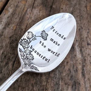 May include: A silver spoon with a floral design and the engraved text "Friends make the world beautiful."