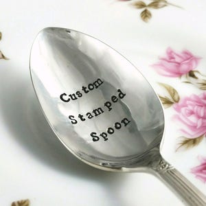 May include: A silver spoon with the words "Custom Stamped Spoon" engraved on the front.
