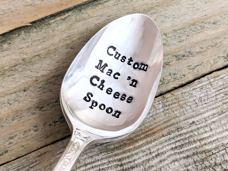 May include: A silver spoon with the words "Custom Mac 'n Cheese Spoon" engraved on the bowl.