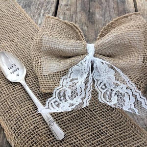 May include: A silver spoon with the words "Let's spoon" engraved on it. The spoon is sitting on a burlap background with a burlap bow and white lace.
