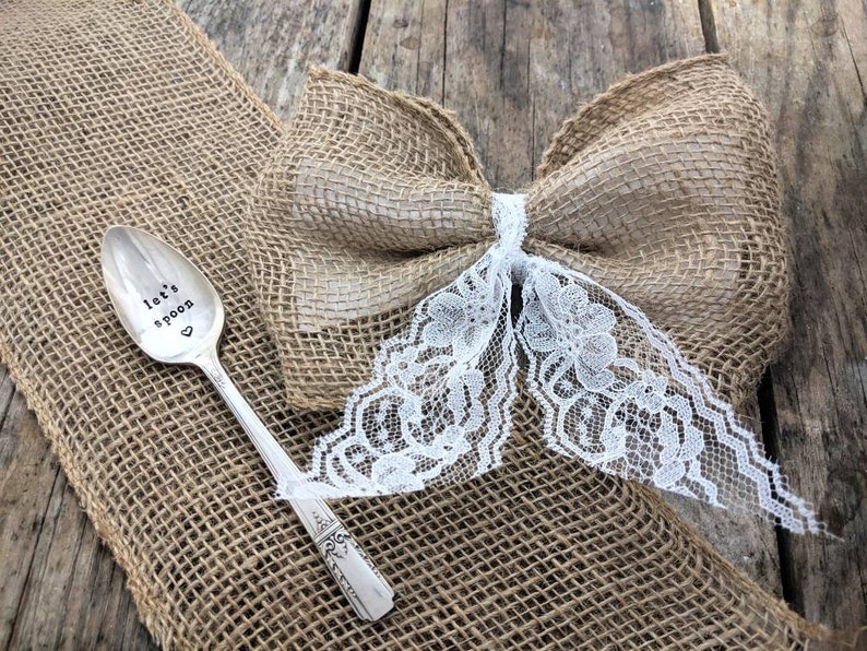 May include: A silver spoon with the words "Let's spoon" engraved on it. The spoon is sitting on a burlap background with a burlap bow and white lace.
