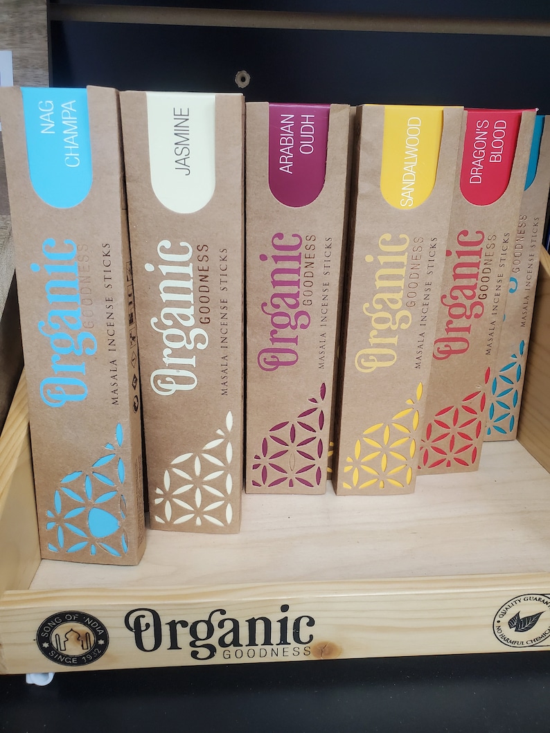 May include: A shelf display of Organic Goodness incense sticks in various scents, including Nag Champa, Jasmine, Arabian Oud, Sandalwood, and Dragon's Blood. The sticks are packaged in brown boxes with a floral design and the brand name.