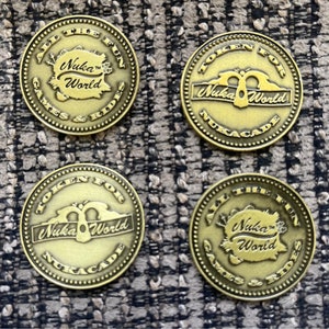 May include: Four gold-colored tokens for the Nuka-World amusement park. Each token features the Nuka-World logo and the text "Token for Nuka-World" or "All the Fun Games & Rides".