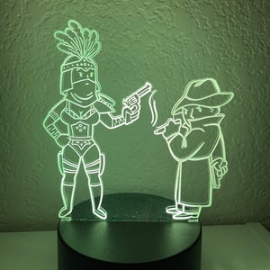 May include: A green light illuminates a 3D printed night light featuring a woman with a feathered headdress holding a gun and a man in a trench coat with a hat.