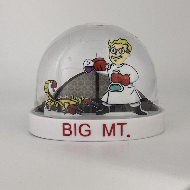 May include: A snow globe with a white base and a clear dome. Inside, a cartoon scientist in a lab coat and a scorpion are featured. The base reads "BIG MT." in red letters.