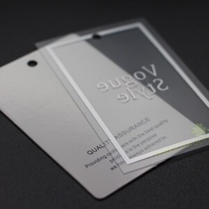 May include: Two rectangular silver tags with a clear plastic overlay. The top tag has the words "Vogue Style" in embossed white letters. The bottom tag has the words "Quality Assurance" and other text.