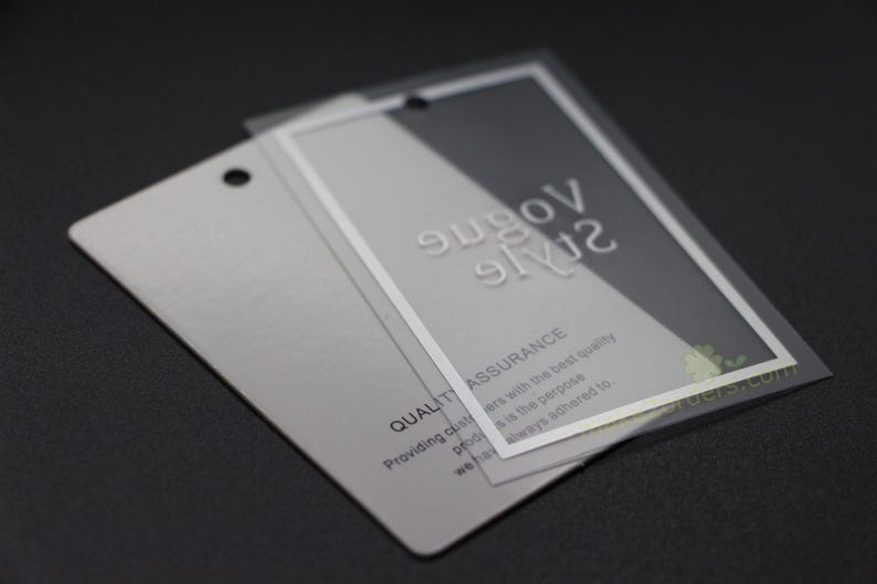 May include: Two rectangular silver tags with a clear plastic overlay. The top tag has the words "Vogue Style" in embossed white letters. The bottom tag has the words "Quality Assurance" and other text.