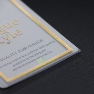 May include: A close-up of a rectangular card with gold lettering and a gold border. The card reads "Vogue Style" and "Quality Assurance". The text below states "Providing customers with the best quality products is the purpose we have always adhered to."