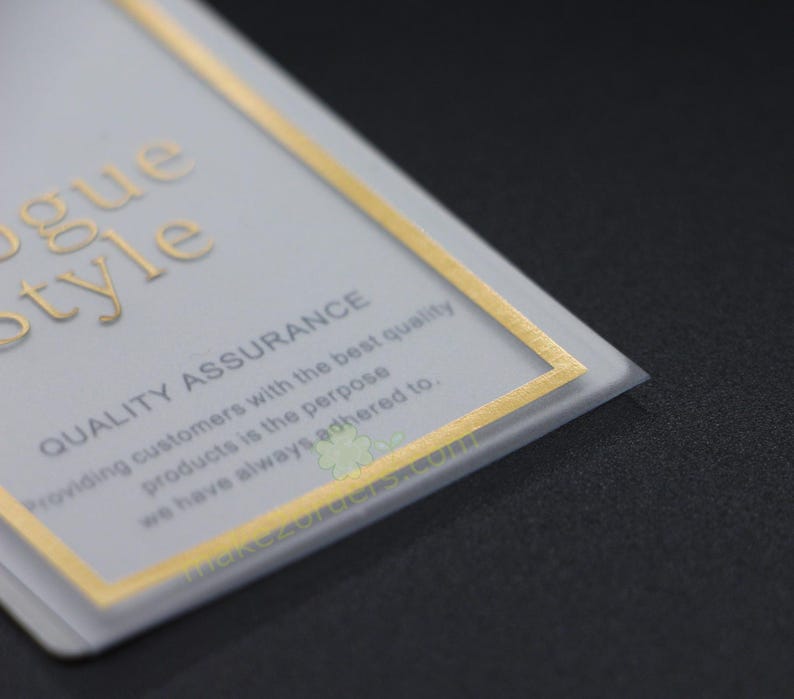 May include: A close-up of a rectangular card with gold lettering and a gold border. The card reads "Vogue Style" and "Quality Assurance". The text below states "Providing customers with the best quality products is the purpose we have always adhered to."