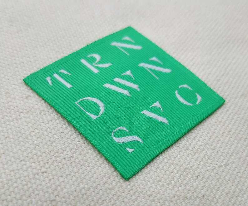 May include: A square, bright green label with white text reading "TRN DWN SVC". The label is made of a ribbed fabric and is set against a neutral, textured background.