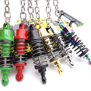May include: A collection of colorful miniature shock absorber keychains. The keychains feature a variety of colors, including green, red, black, gold, silver, and iridescent. Each keychain has a metal spring and a chain for attaching to keys.